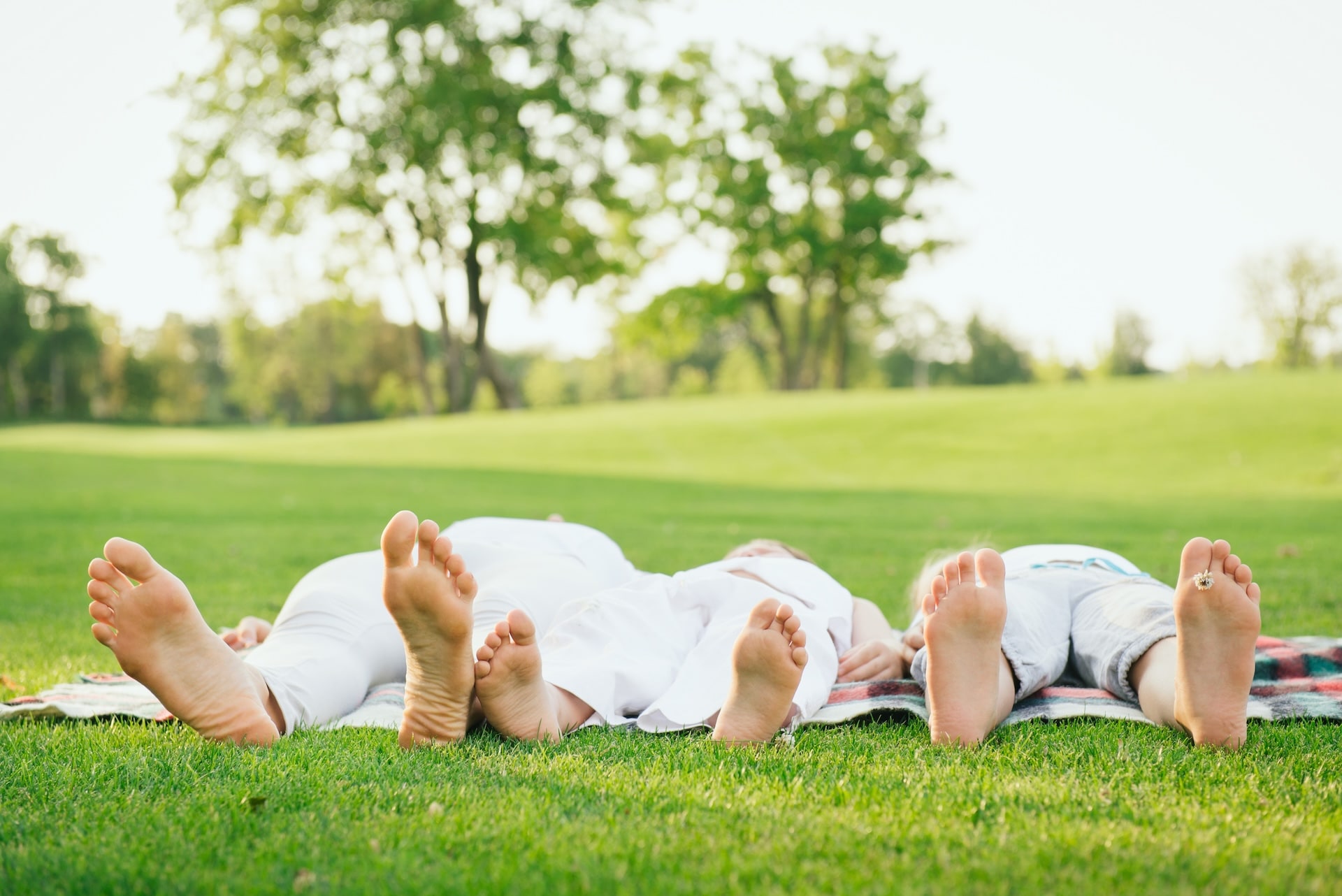Eltern und Kind liegen entspannt nebeneinander auf einer Wiese – Symbol für mehr Ruhe und Verbindung im Familienalltag durch Hypnoparenting