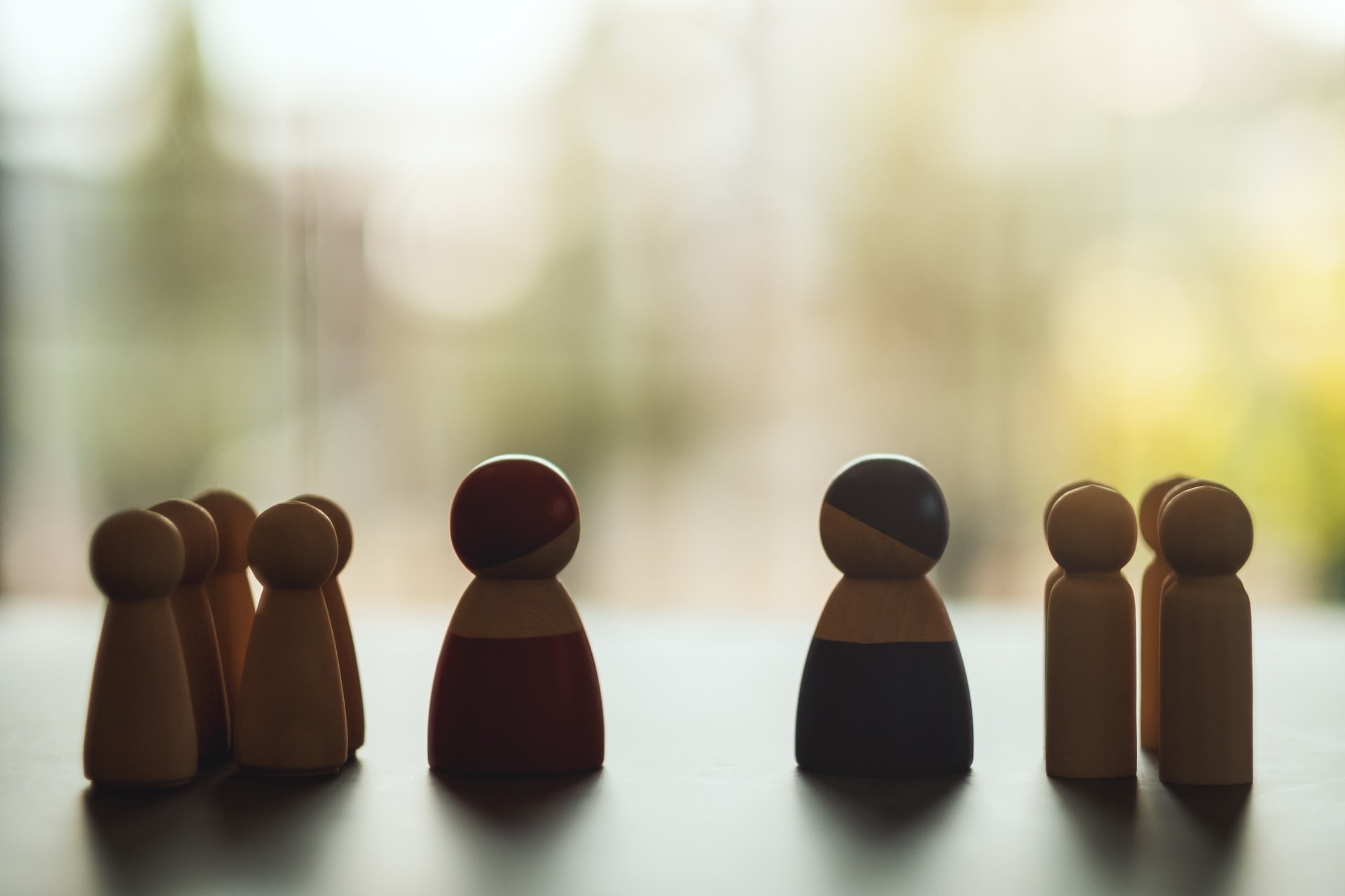 Zwei Gruppen kleiner Holzfiguren stehen sich gegenüber – Symbol für zwei Konfliktparteien, die sich in der Mediation begegnen und gemeinsam eine Lösung finden