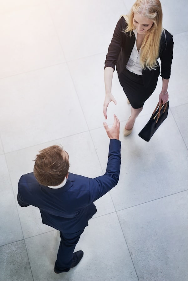 Geschäftsmann und Geschäftsfrau begegnen sich für einen Handschlag in modernem Bürogebäude – Symbol für Augenhöhe, klare Vereinbarungen und vertrauensvolle Zusammenarbeit im Coaching