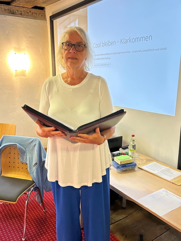 Susanne Smith-Hinz steht mit einer geöffneten Mappe vor den Teilnehmern ihres Workshops.