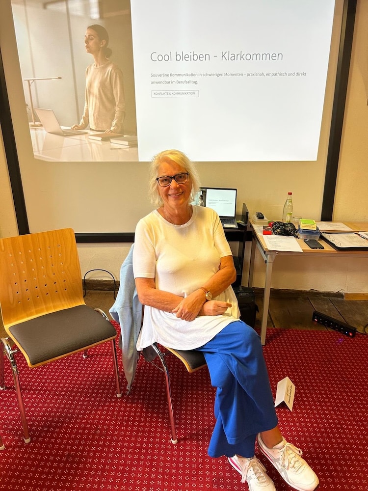 Susanne Smith-Hinz sitzt im Workshopraum vor einer Präsentationswand.